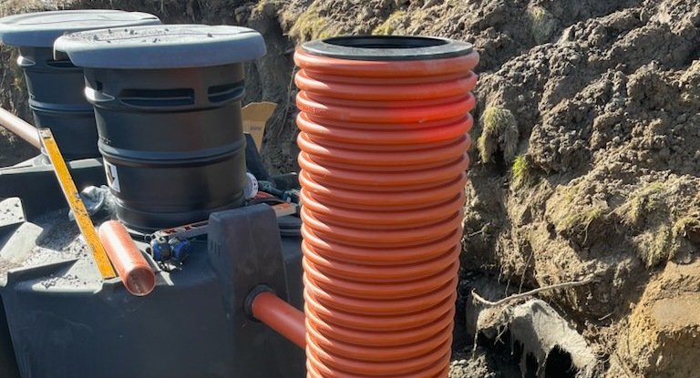 Nedgrävd avloppstank med orange stigarrör och inspektionslock
